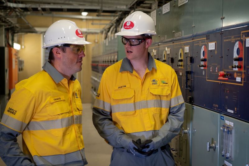Apprentices standing inside a substation near electrical equipment